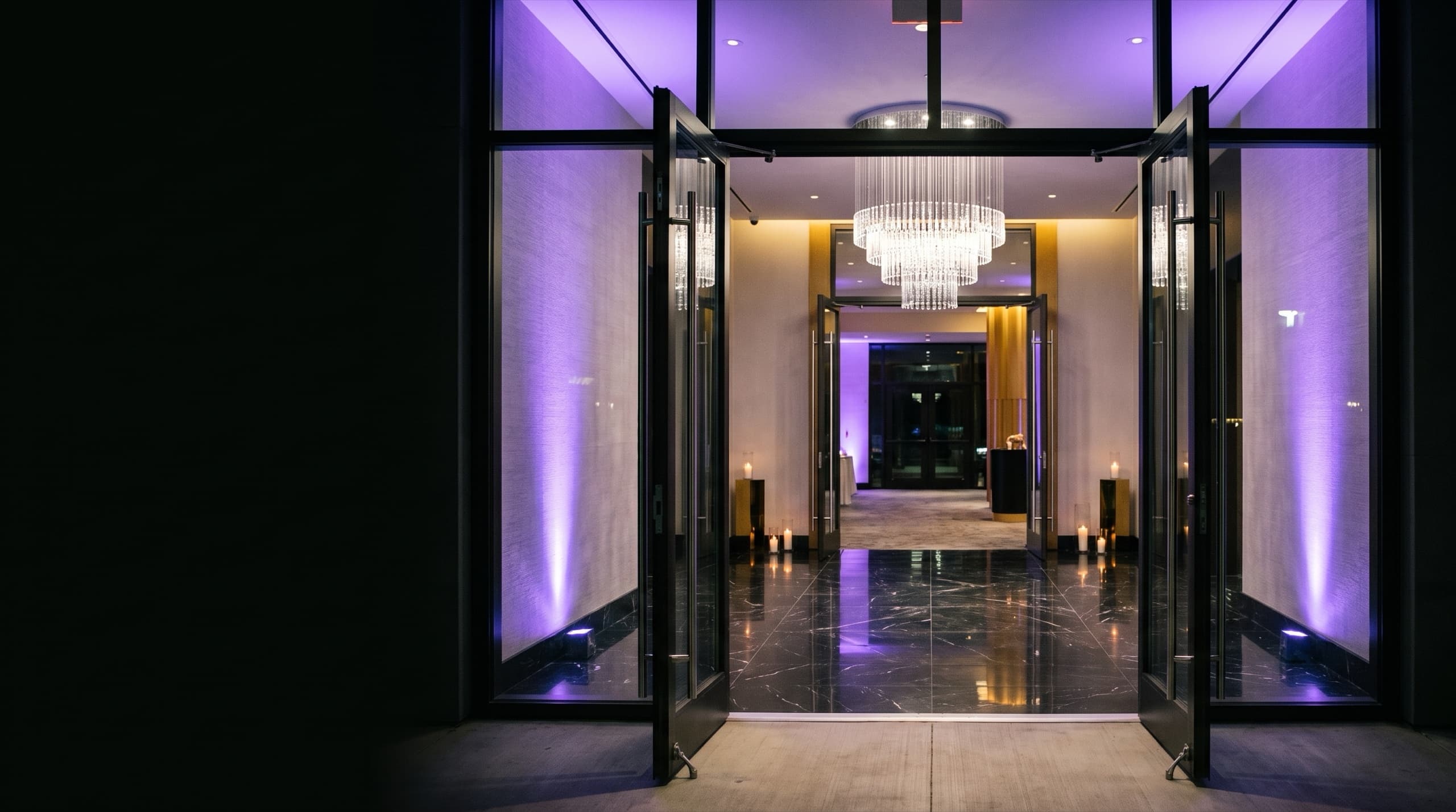 La entrada de un salón de eventos de noche, con las puertas abiertas y las luces encendidas
